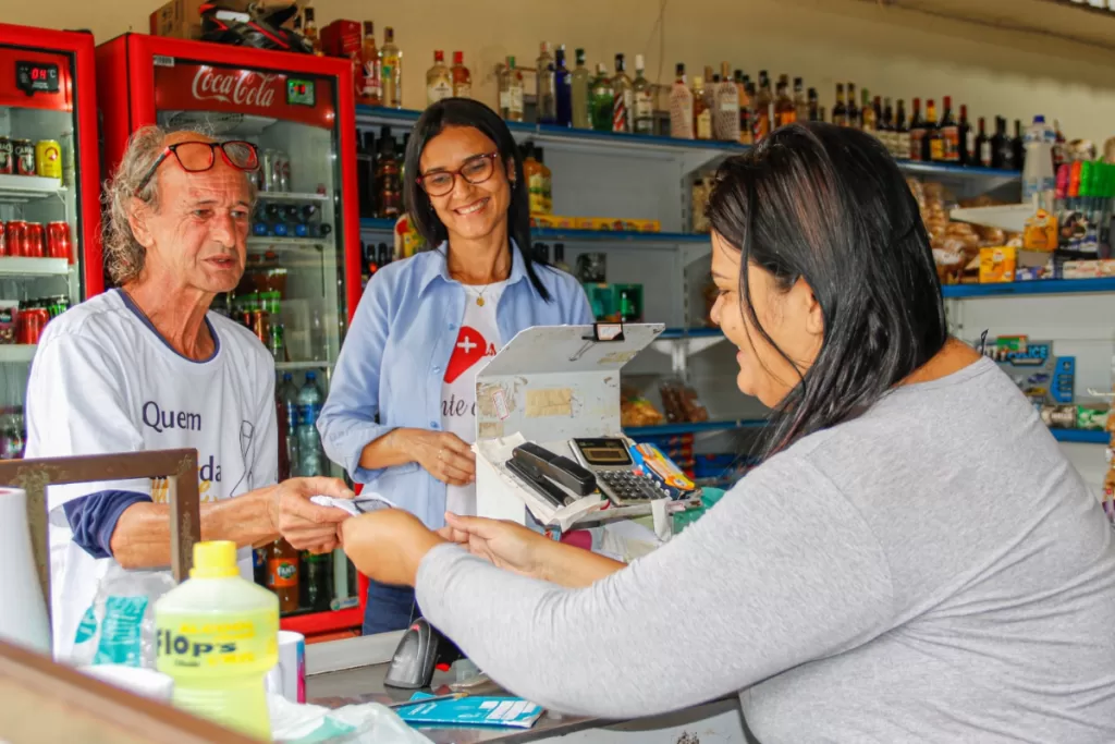 Dois funcionários da área da saúde conversam com a atendente de um caixa de mercadinho em Santa Bárbara.