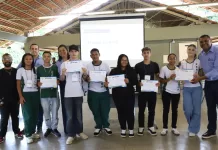 Estudantes com seus certificados em mãos posam para foto ao lado de convidados.