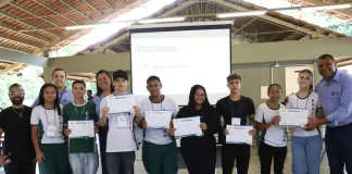 Estudantes com seus certificados em mãos posam para foto ao lado de convidados.