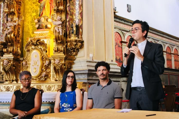 Padre Geraldo fala ao microfone para o público presente.